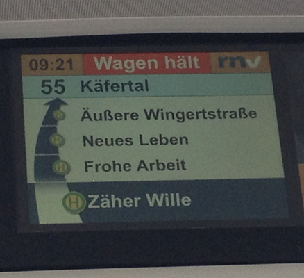Foto einer Haltestellenanzeige eines Mannheimer Busses der Linie 55, darauf sind unter anderem die nächsten drei Haltestellen zu lesen: "Zäher Wille", "Frohe Arbeit" und "Neues Leben".