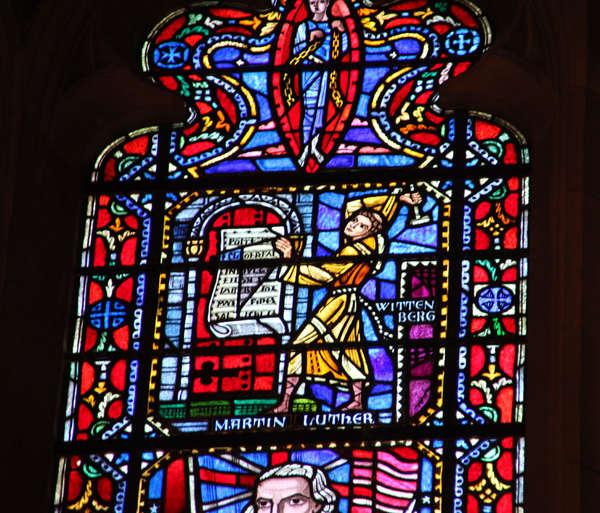 Detail eines Kirchenfensters. Zu sehen ist Martin Luther, der seine 95 Thesen an die Kirchentür in Wittenberg anschlägt.